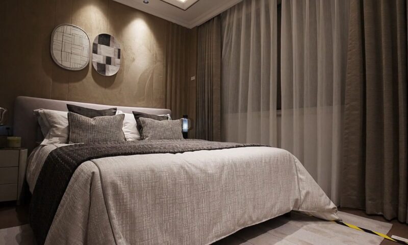 prikaz tamnijeg zida u spavaćoj sobi sivo-krem boje koji je uklopljen sa bojom zavese odmah pored i na sred spavaće sobe veliki bračni krevet